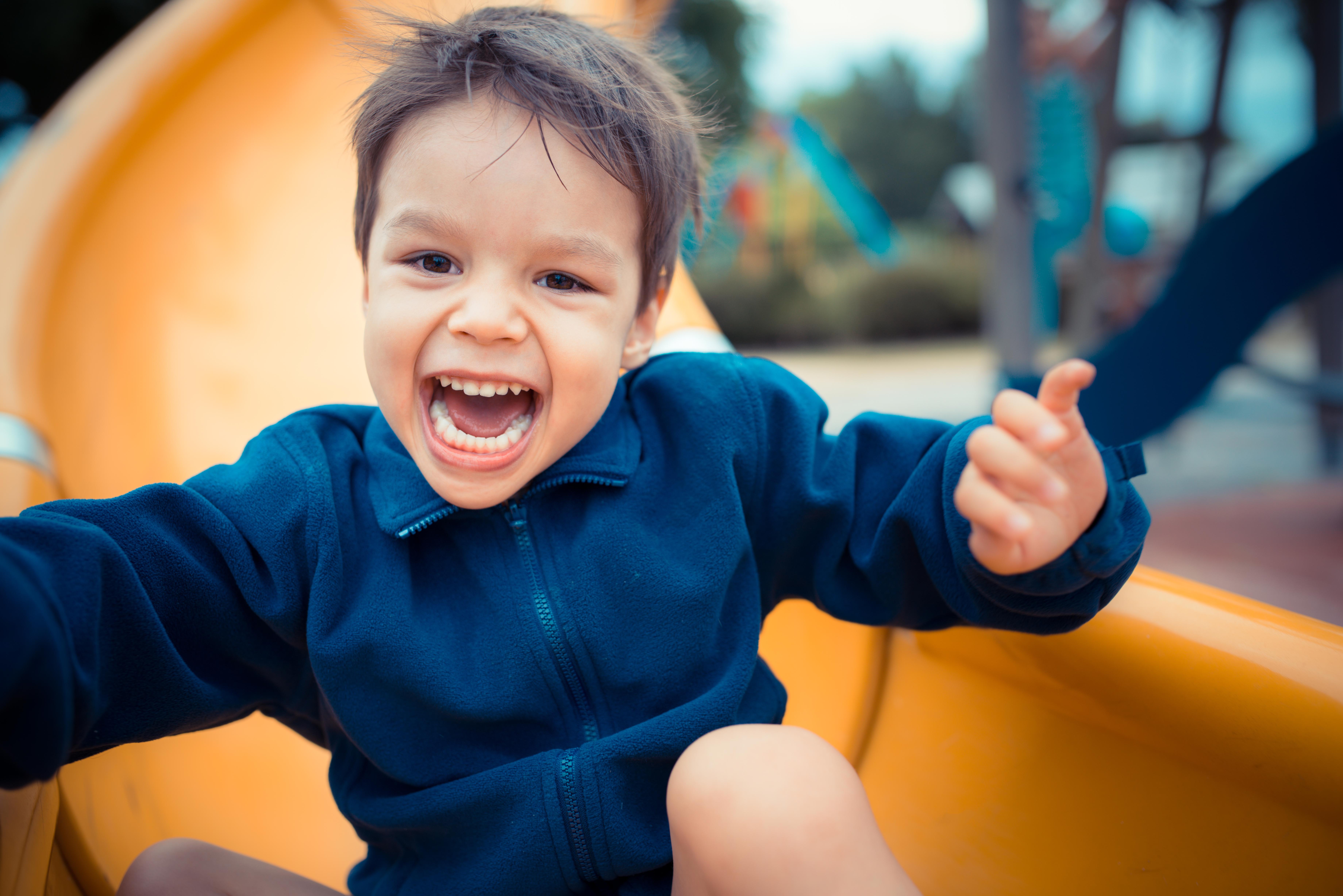 Cute 3 year old Asian boy plays on playground slide